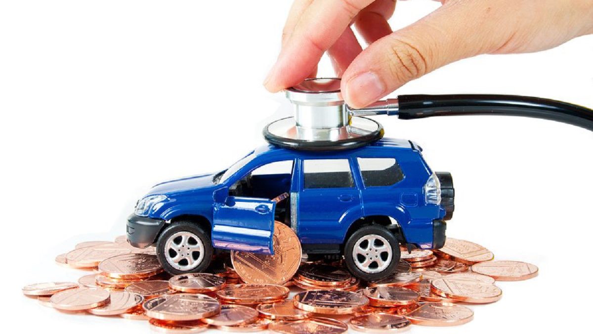  A hand is holding a stethoscope to the roof of a blue toy car sitting on a pile of pennies.